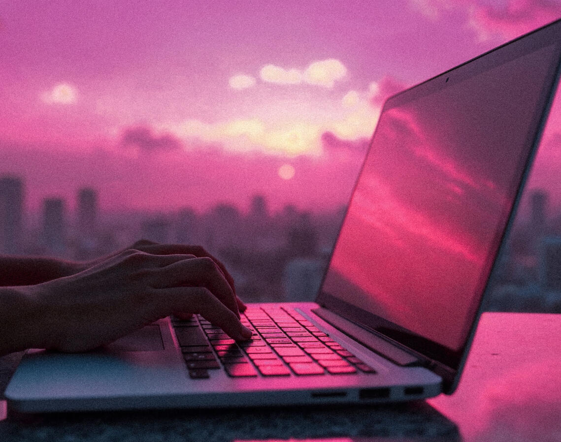 person typing on a laptop with a city skyline in the background